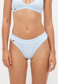 Šviesiai mėlynos bikinio kelnaitės su raukšlėta tekstūra, turinčios plačią juosmenį ir mažą žalią Lacoste logotipą šone.