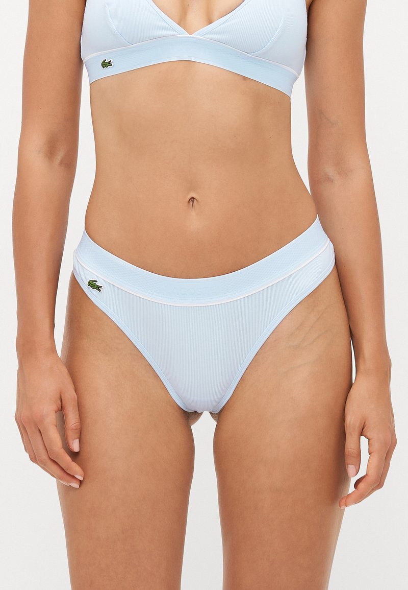 Šviesiai mėlynos bikinio kelnaitės su raukšlėta tekstūra, turinčios plačią juosmenį ir mažą žalią Lacoste logotipą šone.