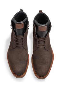 Botas de ante marrón hasta el tobillo con una superficie texturizada, punta redonda y suela de goma marrón. Presentan forro interior negro y acentos decorativos de metal.