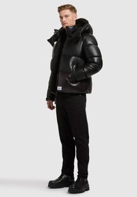 Black padded puffer jacket with a hood, featuring a glossy exterior, side pockets, and a cropped design. Worn with black slim-fit pants and boots.