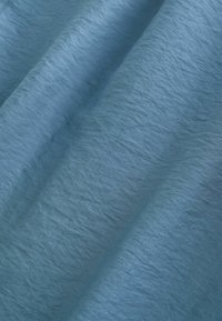 Tissu bleu clair avec une texture subtile et de doux plis créant de délicates ombres sur la surface.