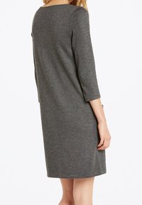 Robe grise, à mi-mollet, fabriquée en tissu doux, avec des manches trois-quarts, un col rond et une coupe décontractée. Aucun motif visible.