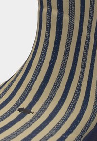 Ύφασμα με κάθετες ριγέ σε μπλε ναυτικό και μπεζ χρώμα, με έναν μικρό μαύρο λεκέ κοντά στην κάτω αριστερή περιοχή.