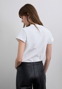 White short-sleeve T-shirt with a round neckline, paired with black fitted faux leather pants featuring two back pockets.