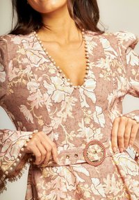 Vestido floral rosa y beige con escote en V, acentos de perlitas en el escote y las mangas, y un detalle decorativo en la hebilla del cinturón.