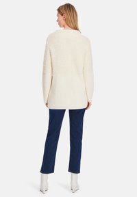 Cream-colored sweater with soft, fluffy texture on top and ribbed knit bottom. Paired with dark blue straight-leg jeans and white ankle boots.