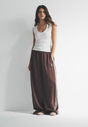 Hvid, ærmeløs top og løse, mørkebrune bukser med hvide striber. Bukserne har elastik i taljen og sidelommer.