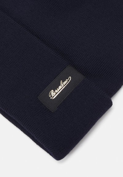 Tamsiai mėlyna megzta kepurė, pasižyminti tekstūruotu paviršiumi ir juodu etiketė su auksinės spalvos įspaudu "Borsalino". Minkšta, tampri medžiaga.