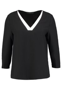 Blusa nera a V con maniche a tre quarti; presenta un accento bianco lungo il collo; tessuto liscio con una vestibilità comoda.