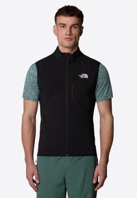 Black sleeveless vest with a high collar and front zipper, made of soft fabric. Features a chest pocket and side pockets.