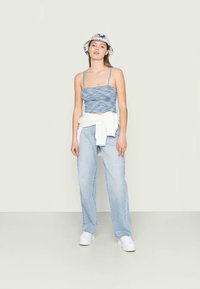 Top curto azul riscado com alças finas, jeans de cintura alta azul claro, sweatshirt branca atada à cintura e ténis brancos.