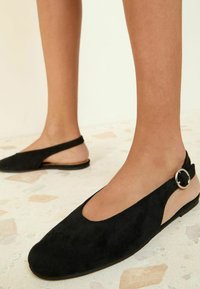 Zwarte suède slingback ballerina's met een ronde neus, voorzien van een uitsnijdingsontwerp en een zilverkleurig rond hardwaredetail op de enkelband.