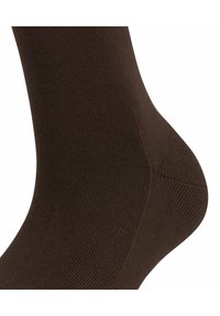 Brūna zeķe ar ribotu tekstūru, ar ciešu piegulšanu un pastiprinātu papēdi. Materiāls izskatās mīksts un elastīgs.