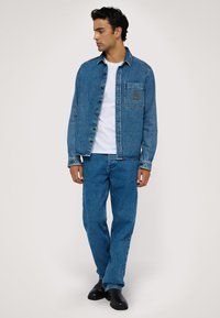 Jeansjacka i medelblått med skalkrage, framficka och knappstängning, tillsammans med matchande jeans och svarta stövlar.