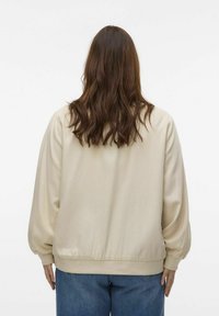 Beige balloon-sleeve jacket with a ribbed hem and cuffs, featuring smooth fabric and a relaxed fit, worn over loose blue jeans.