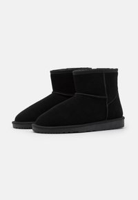 Botines de ante negros con un interior suave, puntera redondeada y suela plana de goma. Incluyen detalles cosidos y un perfil bajo.