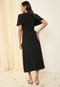 Vestido negro midi con manga corta abullonada, cintura ceñida y cierre de cremallera en la parte posterior. Presenta un tejido suave y una falda recta.