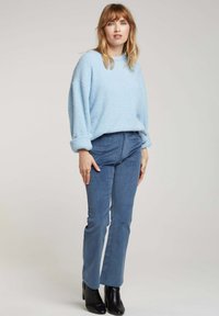 Sweatshirt en polaire bleu clair avec une finition texturée, complété par un pantalon slim-fit bleu foncé et des bottines noires.