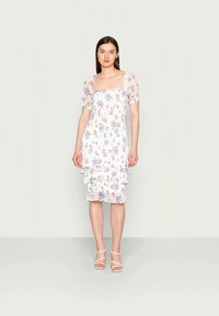 Vestido midi floral em branco, com decote quadrado, mangas curtas bufantes e bainha em camadas com babados. Tecido leve e transparente com padrão floral em tons pastel.