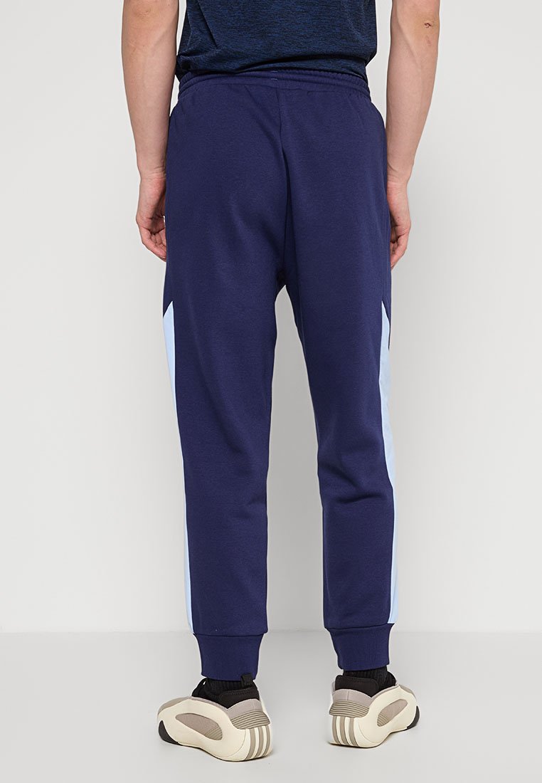 Marineblauwe joggingbroek met lichtblauwe zijkanten, elastische tailleband en bijgesneden enkels, gepaard met beige en zwarte sneakers.