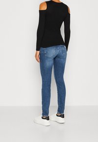 Haut noir à manches longues avec découpes aux épaules dénudées ; assorti à un jean en denim bleu ajusté ; baskets blanches avec détails noirs au talon.