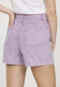 Shorts en denim violet clair avec taille haute, deux poches arrière et un ourlet roulé. Texture lisse avec un détail de couture subtil.