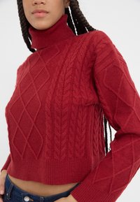 Rode cropped trui met een hoge hals, ingewikkelde kabelpatronen, ribgebreide zomen en een gestructureerd uiterlijk op de mouwen.