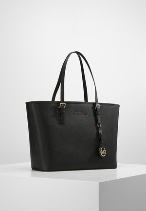 Sac fourre-tout en cuir texturé noir avec double sangle d'épaule, ferrures dorées, et un pendentif rond avec logo MK suspendu à une des sangles.