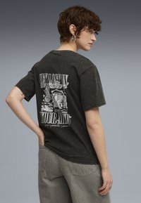 Czarny t-shirt z grafiką w stylu vintage, z wyraźnym białym nadrukiem na plecach, krótkimi rękawami i luźnym krojem.