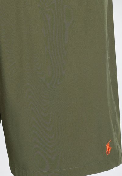 Nahaufnahme von olivgrünem Stoff mit einem orange bestickten Logo eines Polospielers zu Pferd in der unteren rechten Ecke.