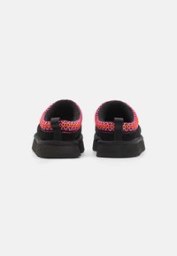 Svarta slip-on skor med en texturerad ovandel som har livliga rosa och orangea vävda detaljer, rundad bakdel och platta gummisulor.