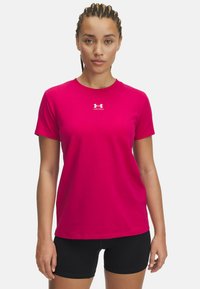 Camiseta ajustada de color rosa brillante de manga corta con cuello redondo, que presenta un pequeño logotipo blanco de Under Armour en el pecho. Textura de tela suave.