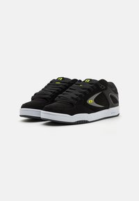 Scarpe atletiche nere con tomaia in suede e materiale sintetico, suola bianca, accenti testurizzati e marchiatura e dettagli in verde neon.
