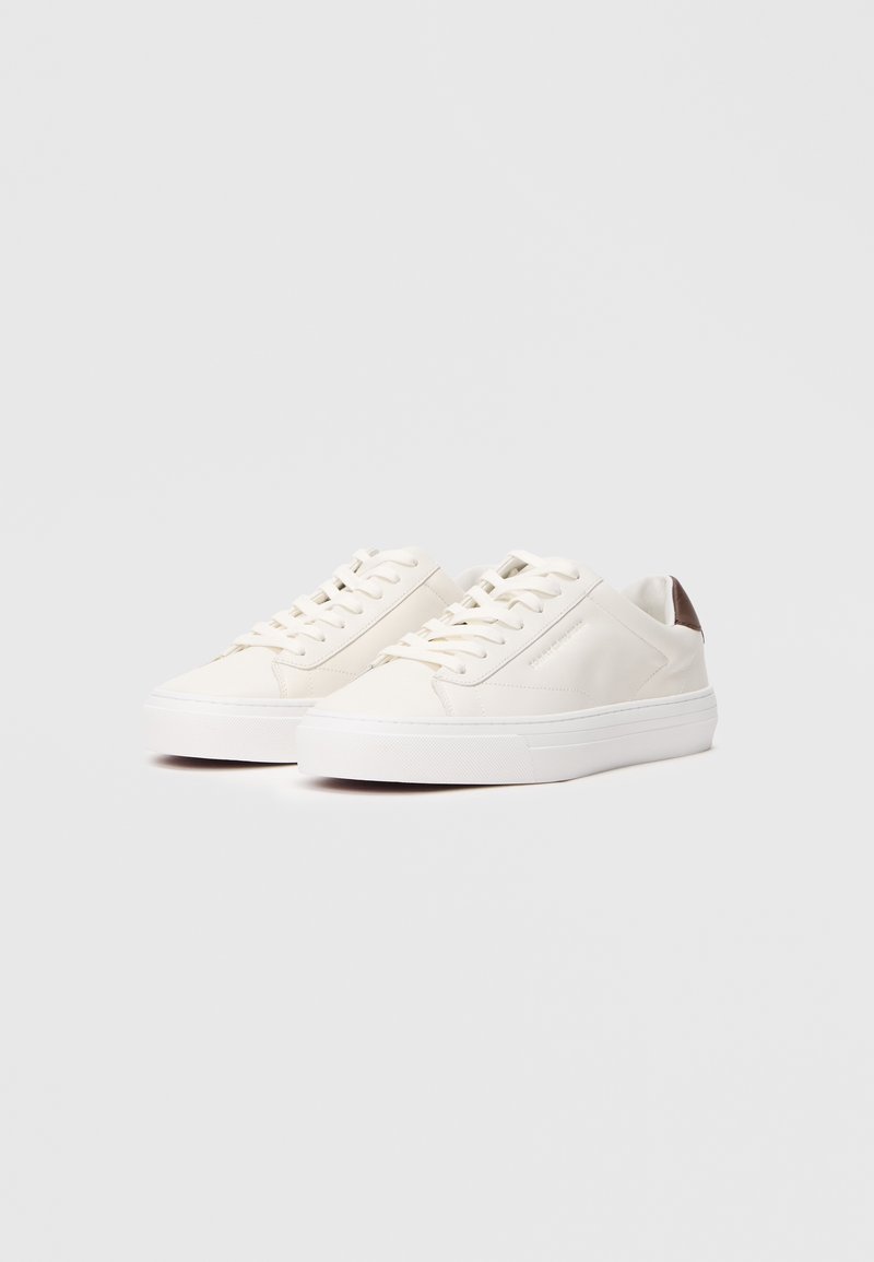 White leather sneakers with a smooth finish, featuring a textured rubber sole and brown accents on the heel and side panel.