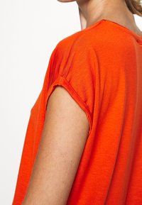 T-shirt orange vif avec une coupe ample, des manches courtes et une texture douce. Les détails de couture sont visibles sur les manches, mettant en valeur le design décontracté.