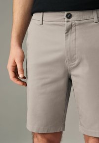 Lys grå shorts lavet af glat stof, med knaplukning foran og sidelommer, der når lige over knæet.