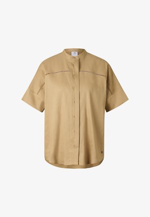 Beżowa koszula na krótki rękaw z guzikami i kołnierzem typu mandarynka oraz poziomymi dekoracyjnymi wycięciami na wysokości klatki piersiowej i na rękawach.