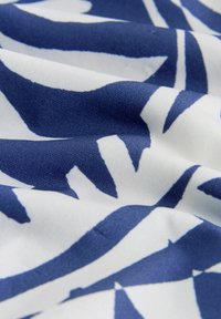 Weißer Stoff mit kräftigen, unregelmäßigen dunkelblauen Blattformen oder abstrakten Mustern, Nahaufnahme zeigt Textur und Falten.