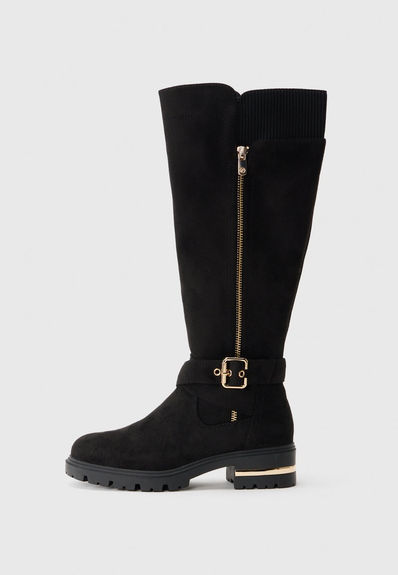 Schwarze Wildleder-Stiefel bis zum Knie mit einem goldenen Reißverschluss, einem Schnallenakzent am Riemen und einer strukturierten Gummisohle. Mit einem gerippten oberen Teil.