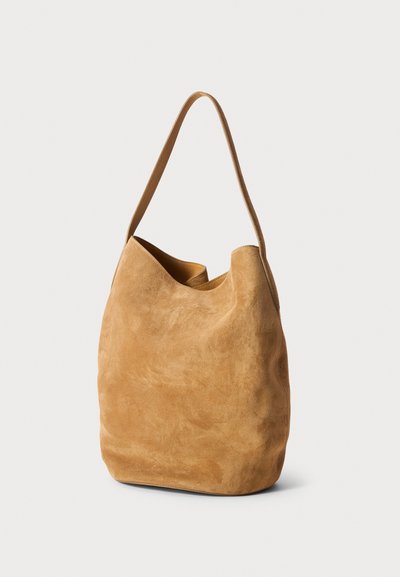 Suede hobo tas in camel kleur, met een enkele schouderband, zachte textuur en een ongestructureerde vorm met een brede opening.