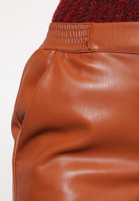 Brun läderkjol med en slät textur. Har en samlad midja och en flödande drapering. Materialet reflekterar ljus något.