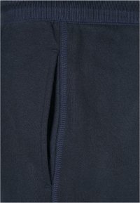 Primer plano de un bolsillo de tela azul marino con costuras visibles y una cinturilla acanalada, mostrando textura y detalles de las costuras.