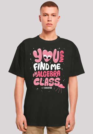 Schwarzes T-Shirt mit kurzen Ärmeln, das ein buntes Grafikdesign zeigt. Der Text lautet "DU FINDEST MICH IM ALGEBRAUNTERRICHT" und zeigt verspielte Alien- und Planetenmotive.