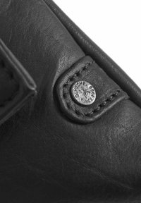 Detail na čiernej koženej topánke s hladkým povrchom, prešitým dielom s kovovým logom a zakrivenými dizajnovými prvkami.