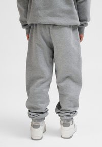 Graue Sweatpants mit elastischen Bündchen an den Knöcheln, aus weichem Stoff. Tragen mit hellen Sneakers mit grauen Akzenten.