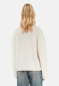 Sweatshirt surdimensionné de couleur crème avec un col arrondi et une bordure côtelée. Comprend des manches raglan et un tissu doux et texturé.