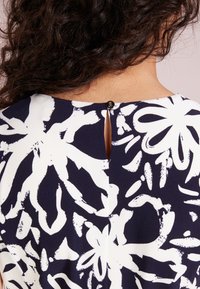 Abito navy con stampa floreale bianca, chiusura con bottoni sul retro, dettaglio a fessura e un tessuto liscio e testurizzato.