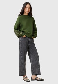 Olivgrön oversized sweatshirt med sänkta axlar, kombinerad med högmidjade svarta jeans med synliga sömmar och fransade fållar.