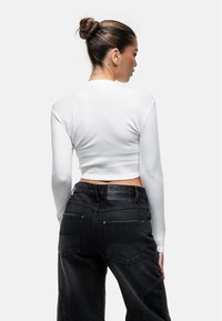 Weißes, kurzes Oberteil mit langen Ärmeln, kombiniert mit hochgeschnittenen schwarzen Jeans mit strukturierter Oberfläche und sichtbaren Nähten.