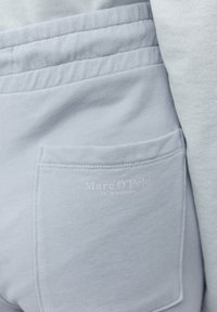 Světle modrá mikina s hladkou texturou, žebrovaným límcem a přišitým bočním kapsou s logem v bledém potisku.